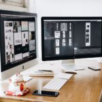 Web design workspace with dual monitors displaying UI layouts for web design and graphic design projects.