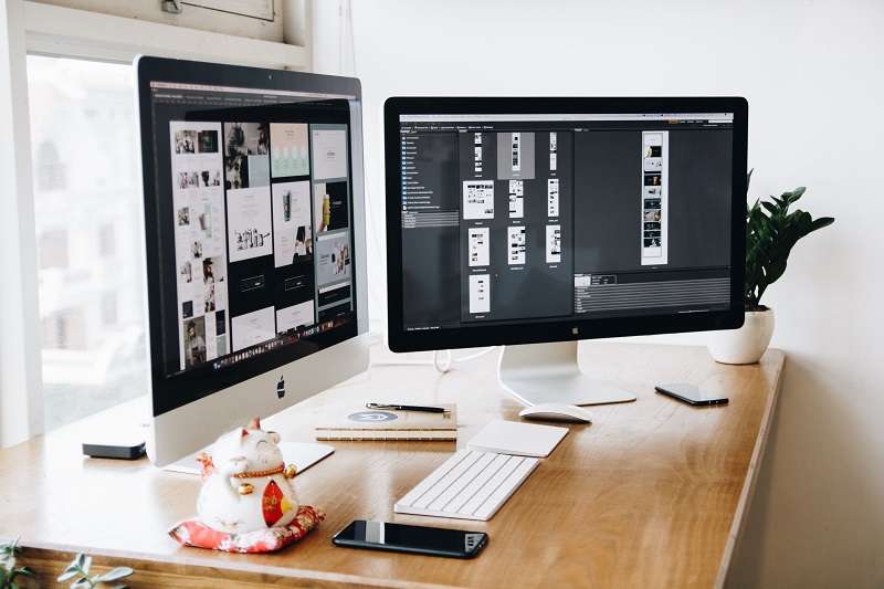 Web design workspace with dual monitors displaying UI layouts for web design and graphic design projects.