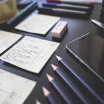 Web design wireframes, pencils, and a smartphone arranged on a desk during website planning.