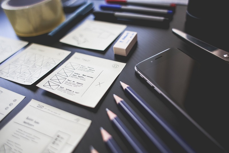 Web design wireframes, pencils, and a smartphone arranged on a desk during website planning.